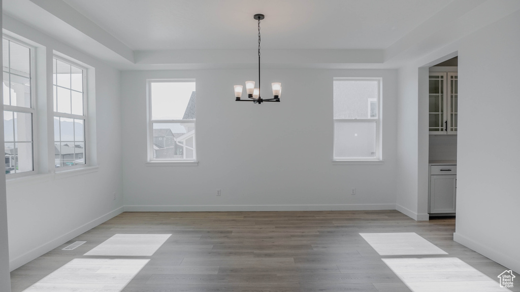 Unfurnished dining area featuring a chandelier, light wood-type flooring, and a raised ceiling