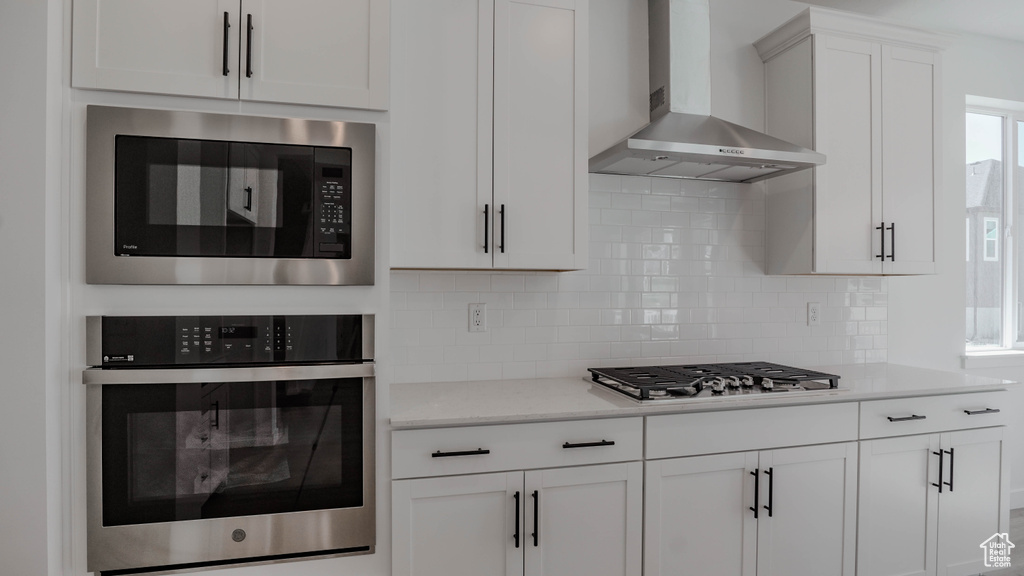 Kitchen with stainless steel appliances, wall chimney range hood, light countertops, tasteful backsplash, and white cabinets
