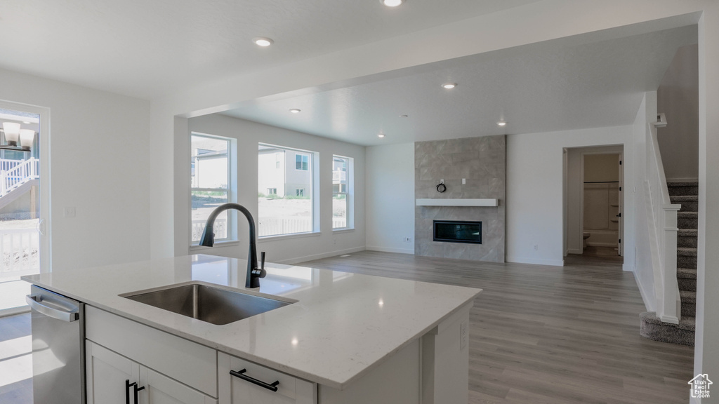 Kitchen with stainless steel dishwasher, light wood-style floors, white cabinetry, light stone countertops, and a tiled fireplace
