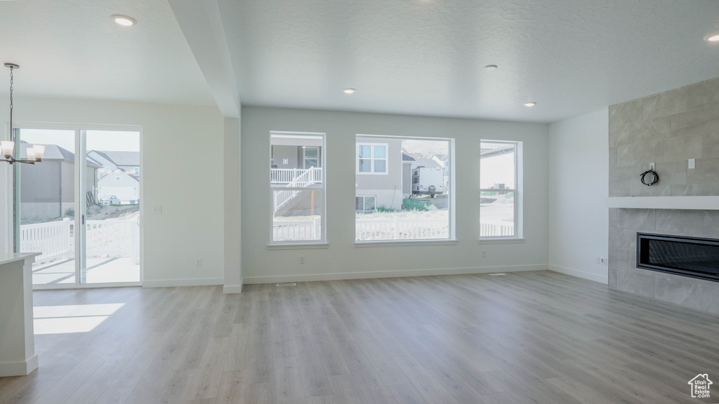 Unfurnished living room with healthy amount of natural light, a tile fireplace, light wood-style flooring, a chandelier, and recessed lighting