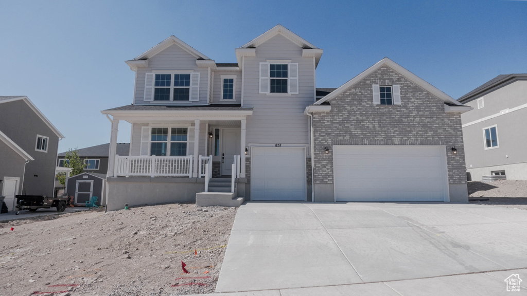 View of front of house featuring a porch, a garage, driveway, brick siding, and a storage unit