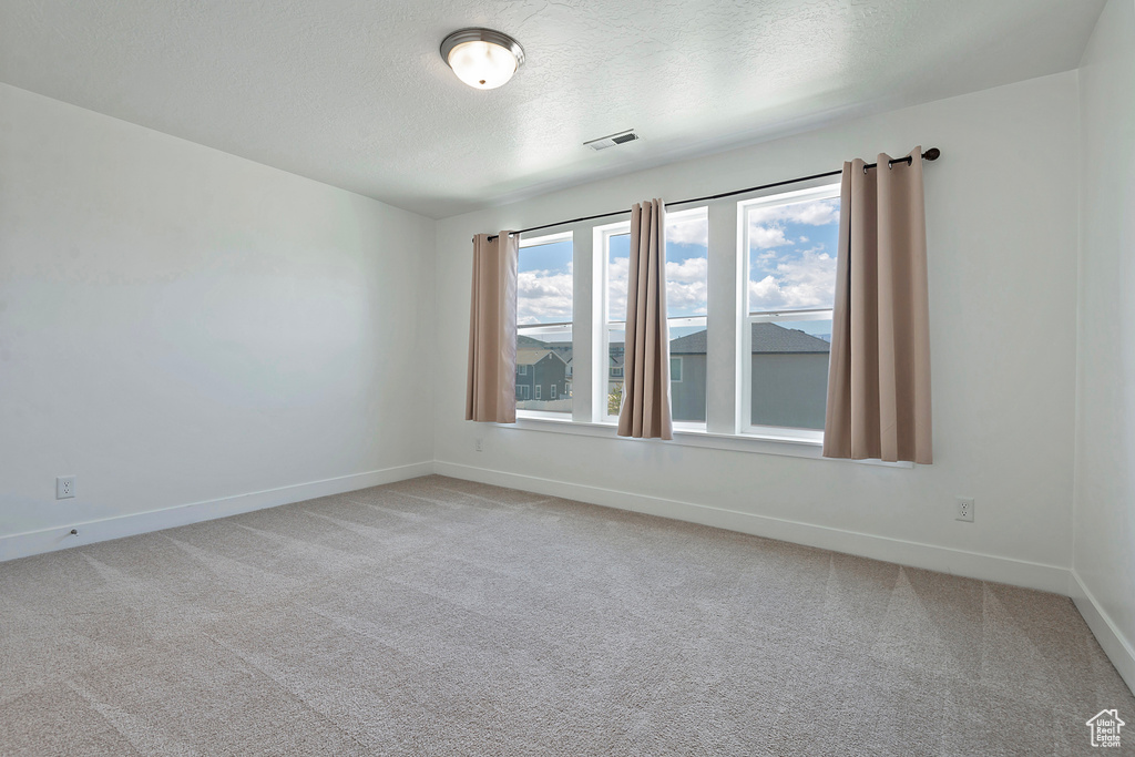 Empty room with baseboards, light colored carpet, visible vents, and a textured ceiling