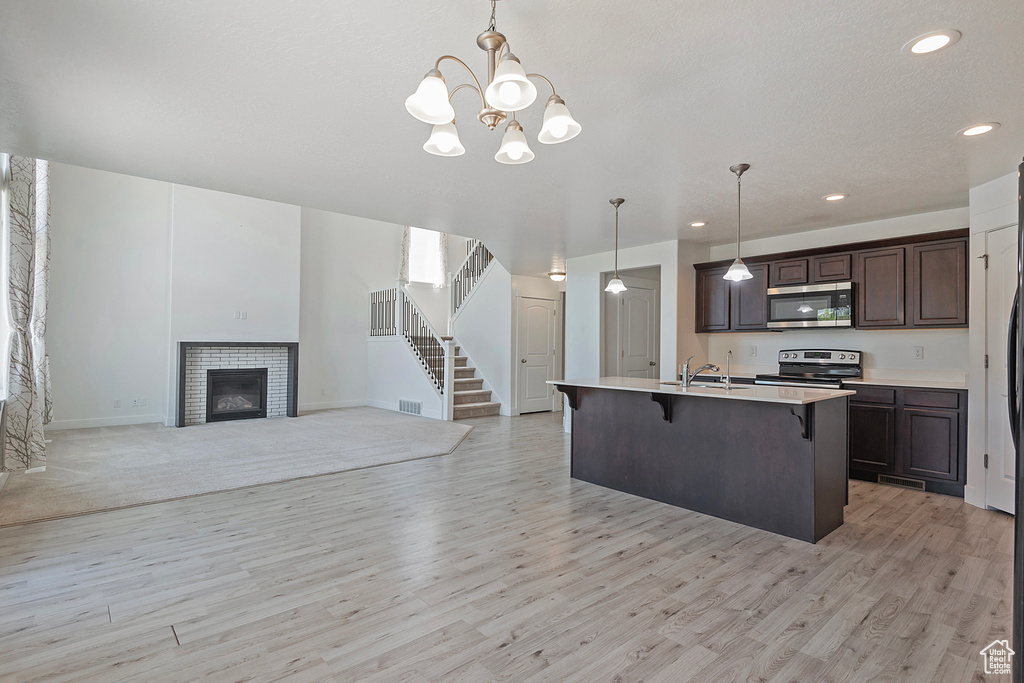 Kitchen featuring dark brown cabinetry, a kitchen breakfast bar, a sink, light wood-style flooring, and appliances with stainless steel finishes