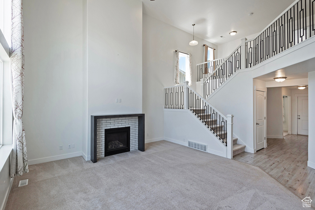 Unfurnished living room with carpet flooring, a high ceiling, baseboards, visible vents, and stairway