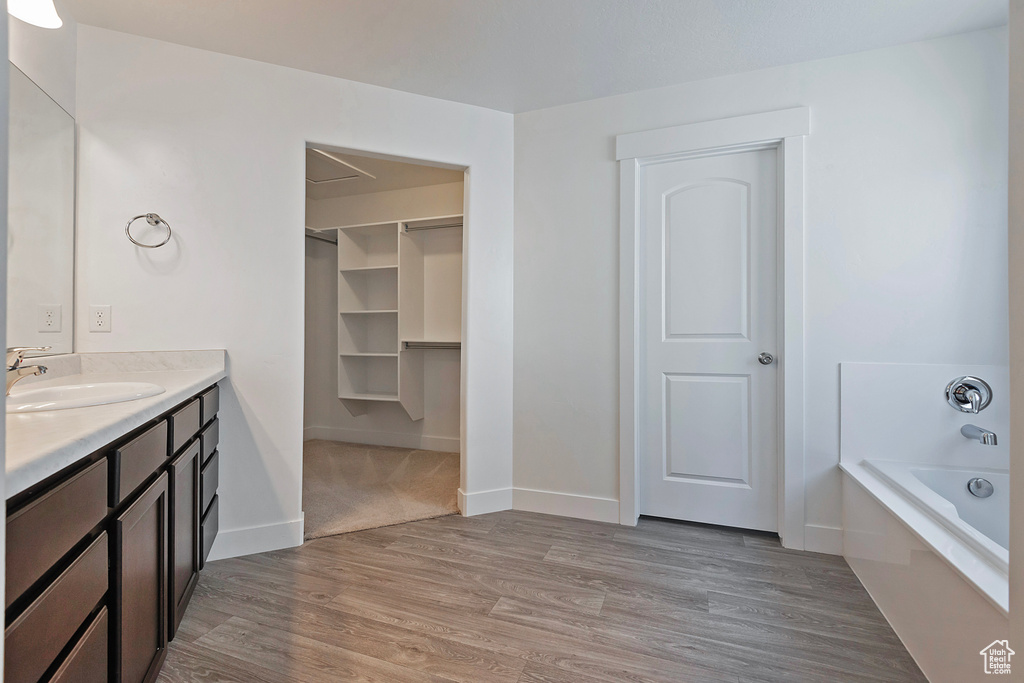 Bathroom featuring baseboards, wood finished floors, a garden tub, and vanity