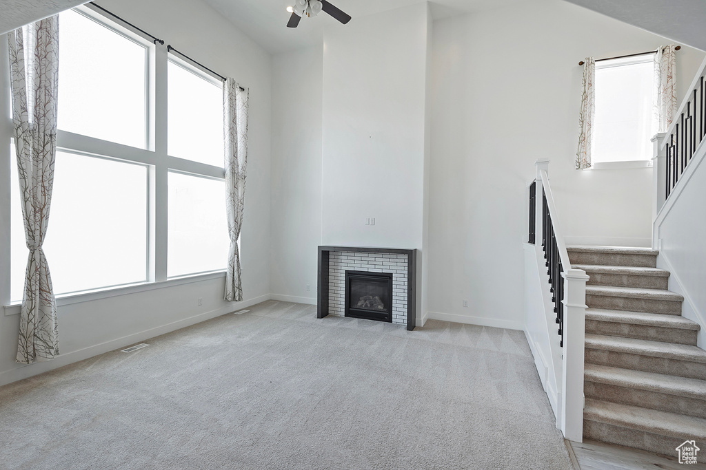 Unfurnished living room with stairs, a ceiling fan, light carpet, and a wealth of natural light