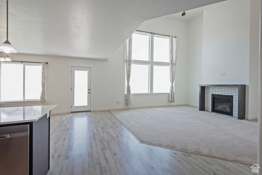 Unfurnished living room featuring baseboards, a brick fireplace, light wood finished floors, and a textured ceiling