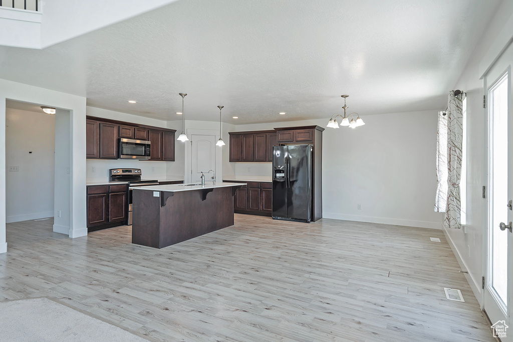 Kitchen with light wood finished floors, a breakfast bar area, stainless steel appliances, visible vents, and a center island with sink