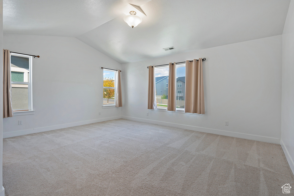 Empty room featuring a healthy amount of sunlight, baseboards, vaulted ceiling, and visible vents