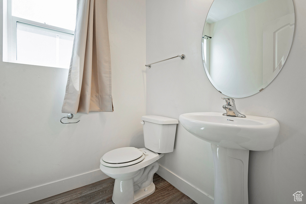 Half bath featuring toilet, wood finished floors, baseboards, and a sink