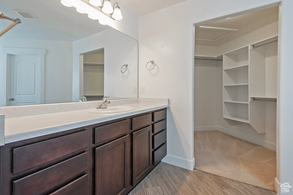 Full bath with vanity, baseboards, wood finished floors, a spacious closet, and visible vents