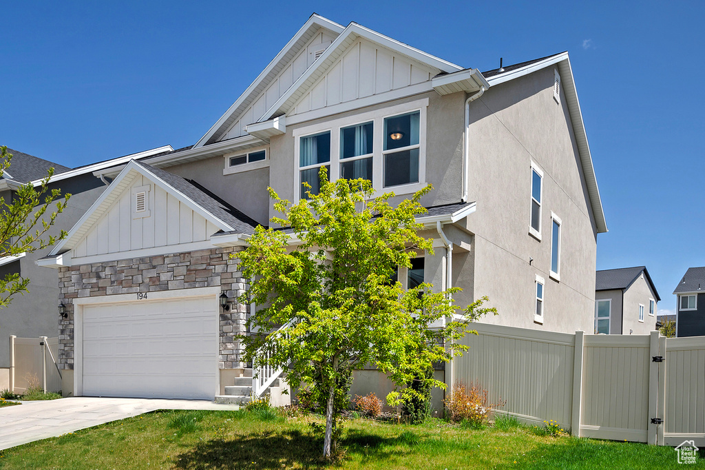 Craftsman house with board and batten siding, driveway, stone siding, and fence