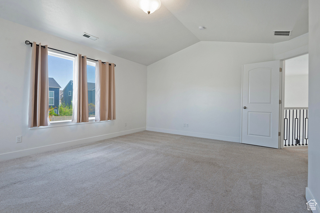 Carpeted empty room featuring visible vents, baseboards, and lofted ceiling