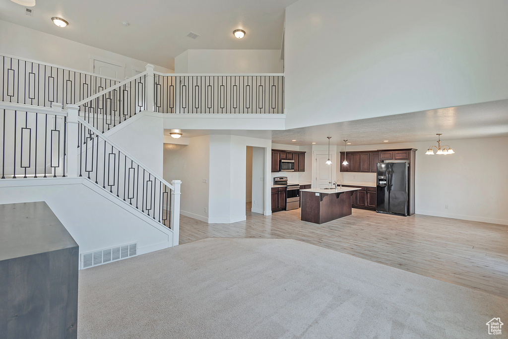 Unfurnished living room featuring visible vents, baseboards, a chandelier, a high ceiling, and light wood-style flooring
