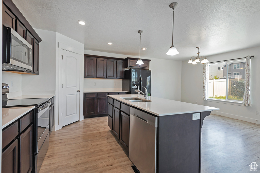 Kitchen with dark brown cabinets, light countertops, a textured ceiling, light wood-style flooring, and stainless steel appliances
