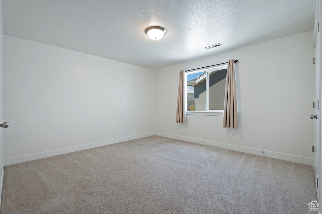 Empty room with light colored carpet, a textured ceiling, baseboards, and visible vents