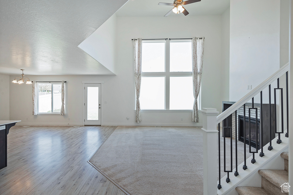 Unfurnished living room featuring baseboards, ceiling fan with notable chandelier, wood finished floors, and stairway