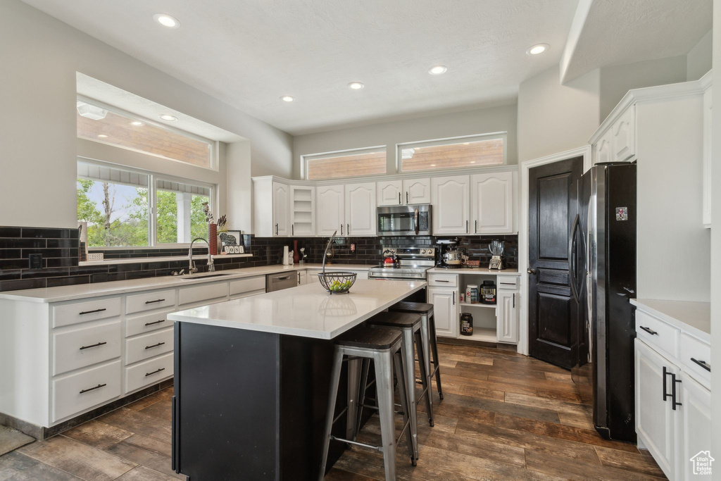 Kitchen with stainless steel appliances, a sink, tasteful backsplash, a breakfast bar, and white cabinets