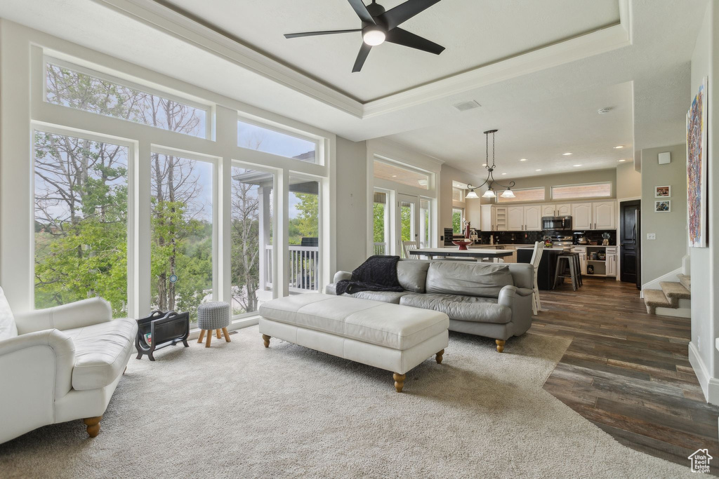 Living room featuring dark wood-type flooring, ceiling fan, ornamental molding, a tray ceiling, and recessed lighting