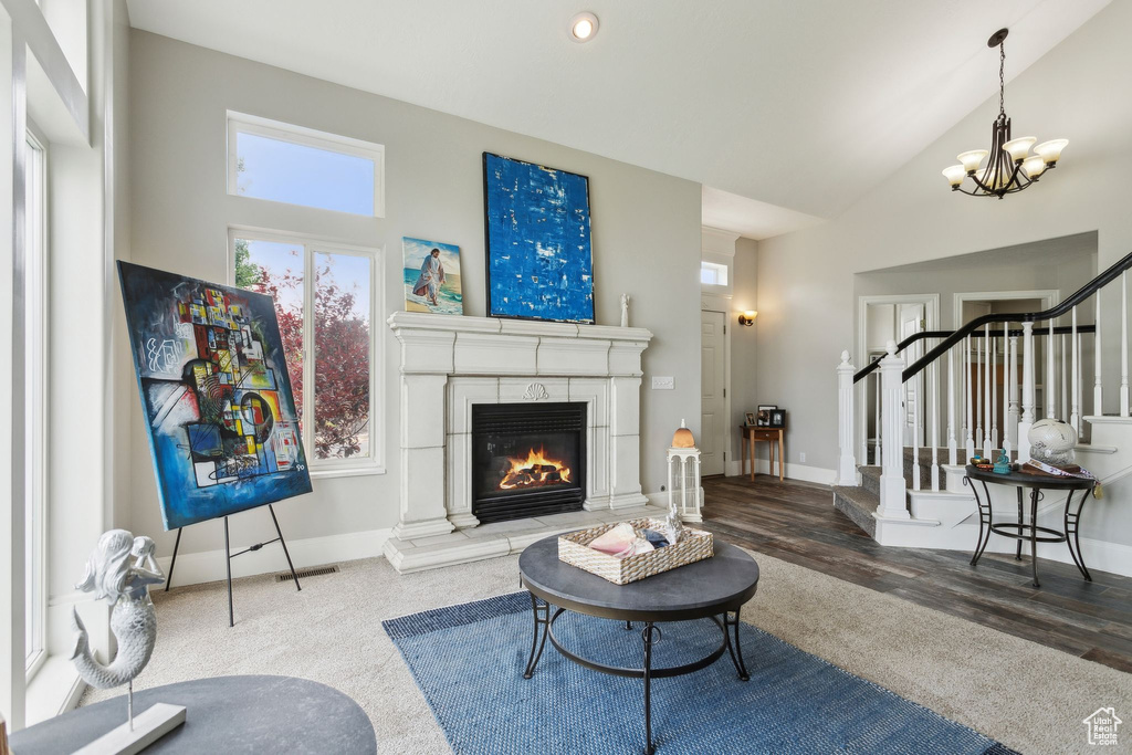Living room featuring stairway, a chandelier, a glass covered fireplace, high vaulted ceiling, and baseboards