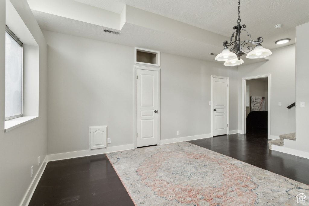 Spare room with dark wood-style floors, a chandelier, baseboards, and stairs