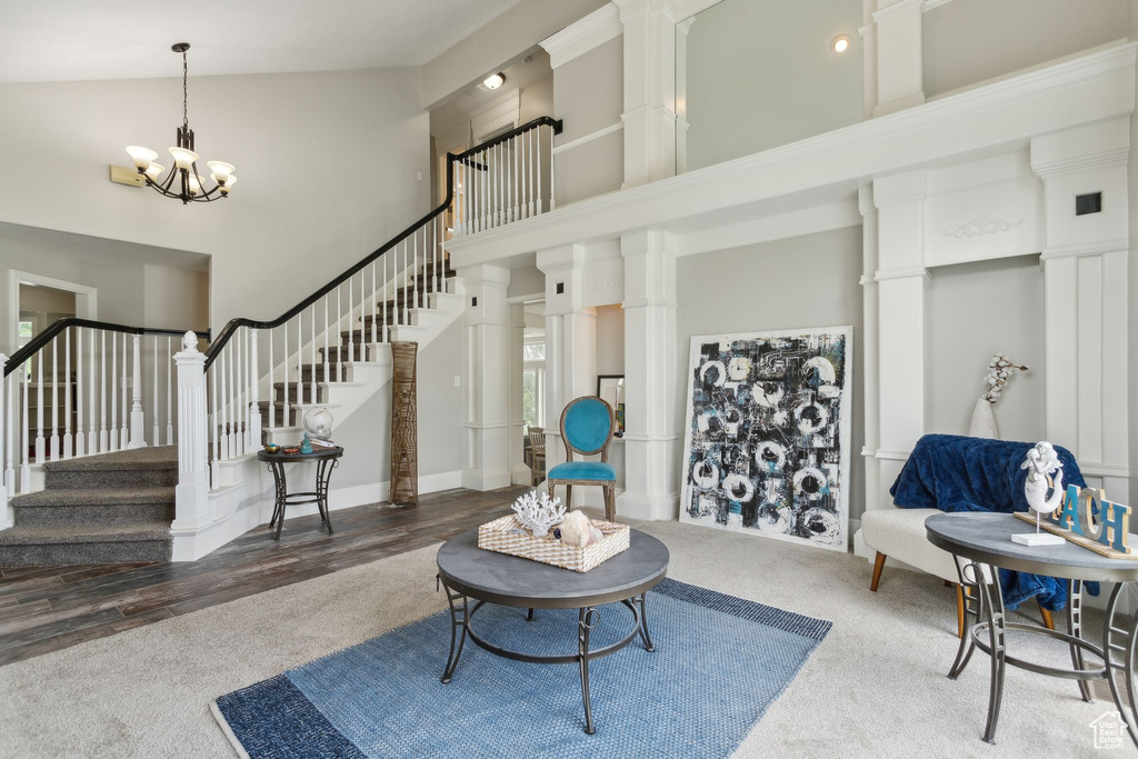 Living room featuring a towering ceiling, a chandelier, stairs, carpet flooring, and decorative columns