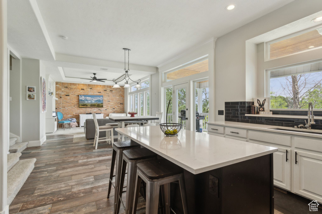 Kitchen featuring a sink, a kitchen island, dark wood finished floors, light countertops, and open floor plan