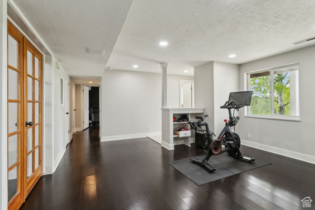 Exercise room featuring a textured ceiling, recessed lighting, baseboards, dark wood-style floors, and decorative columns