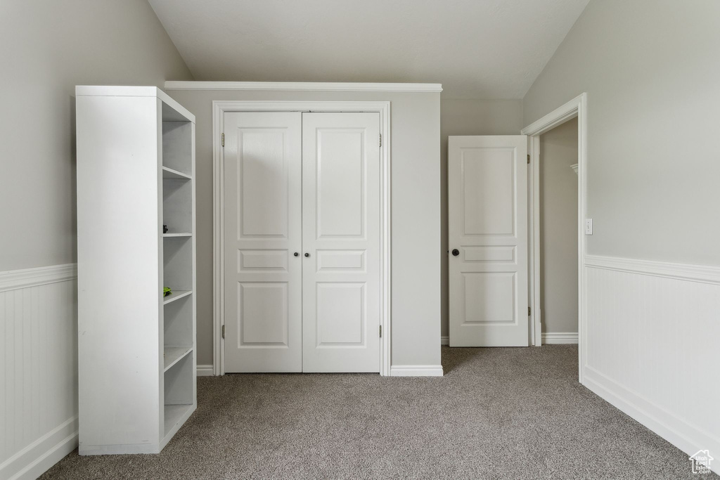 Unfurnished bedroom featuring a wainscoted wall, a closet, carpet, and vaulted ceiling