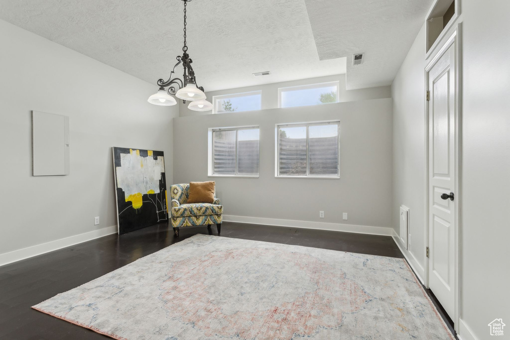 Living area with a textured ceiling, a chandelier, dark wood finished floors, and baseboards