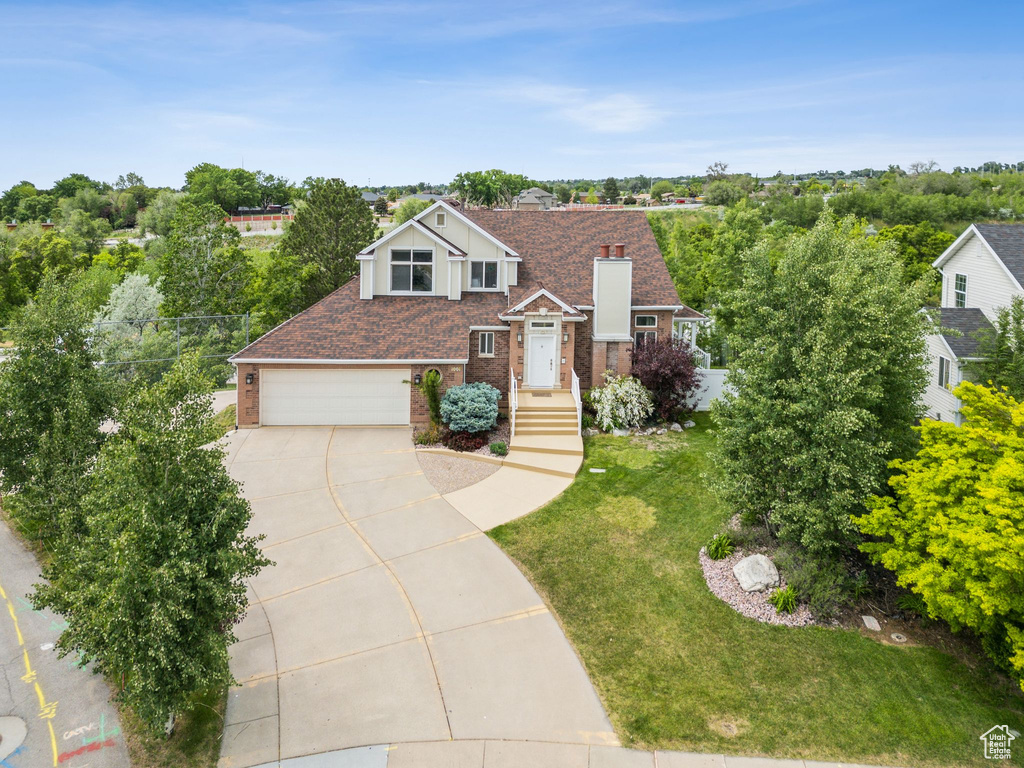 View of front of home featuring concrete driveway, brick siding, a front yard, a chimney, and an attached garage