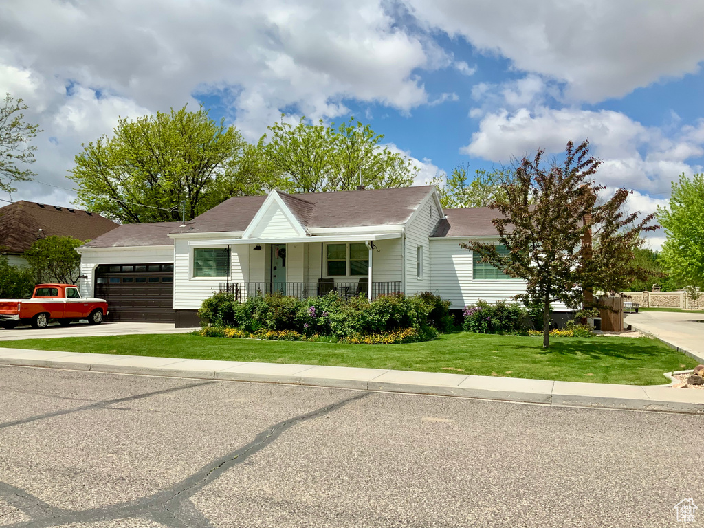 View of front facade featuring a garage, a porch, a front lawn, concrete driveway, and roof with shingles