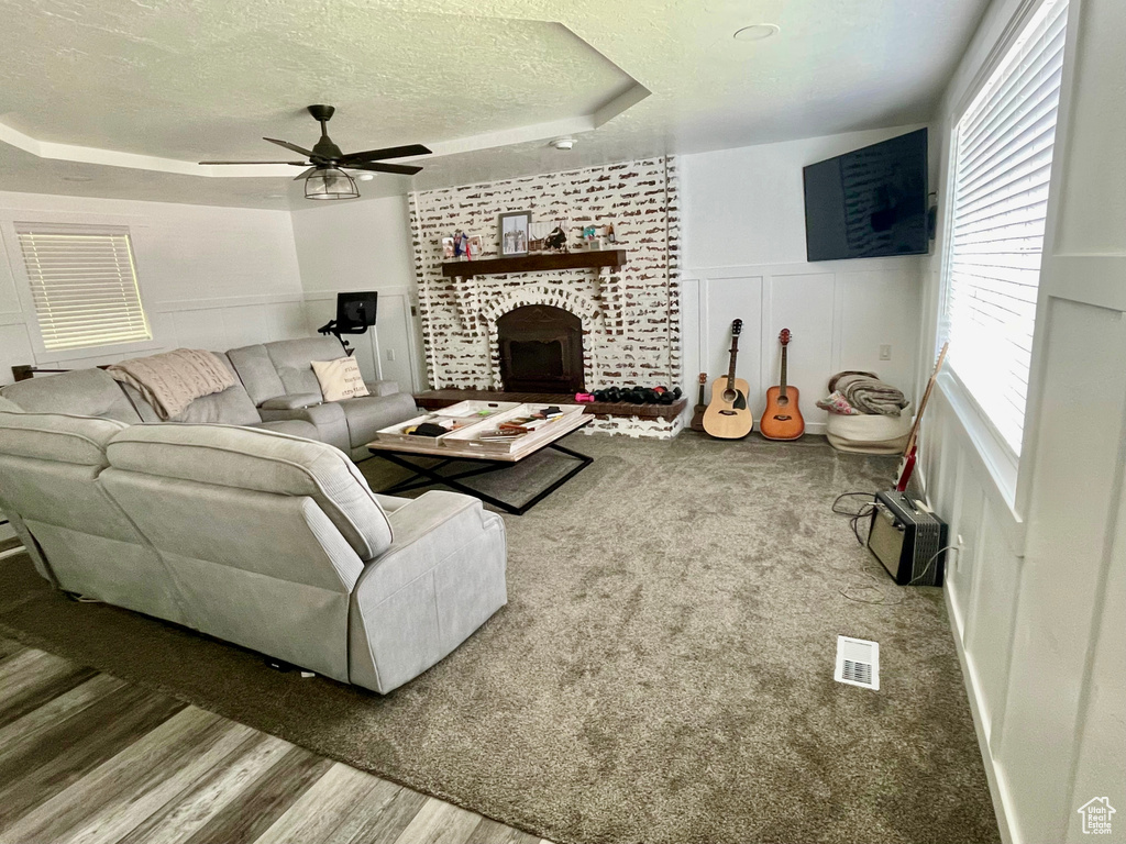 Living room featuring a textured ceiling, a raised ceiling, ceiling fan, a decorative wall, and plenty of natural light