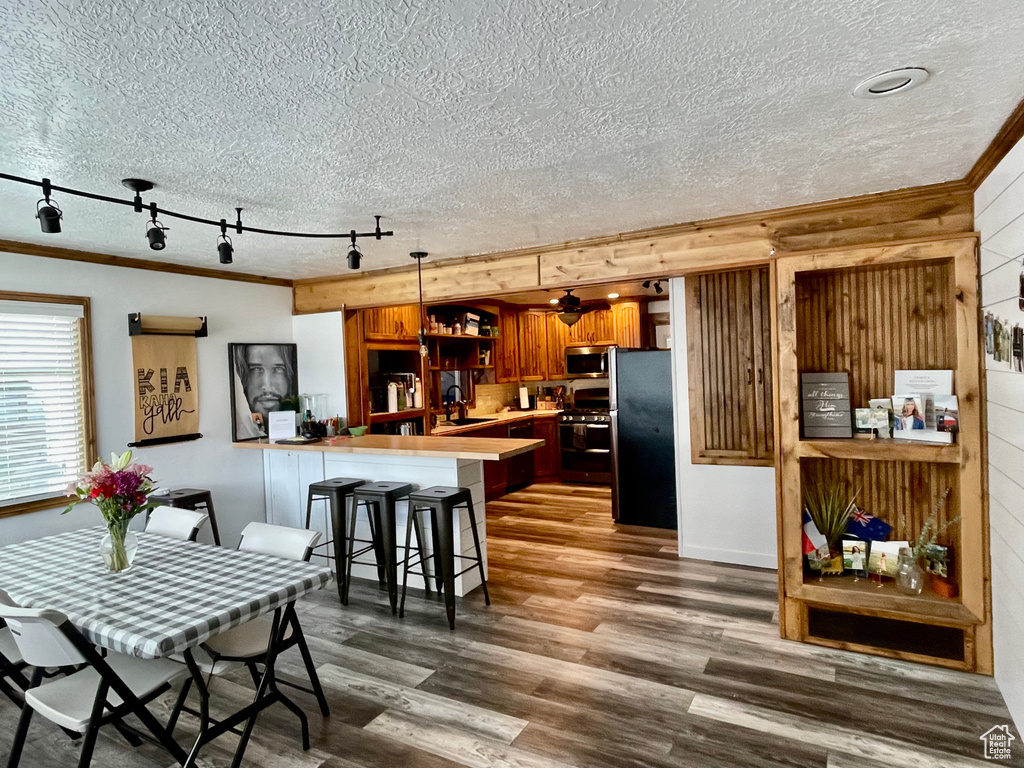 Dining area featuring a textured ceiling, wooden walls, crown molding, rail lighting, and wood finished floors