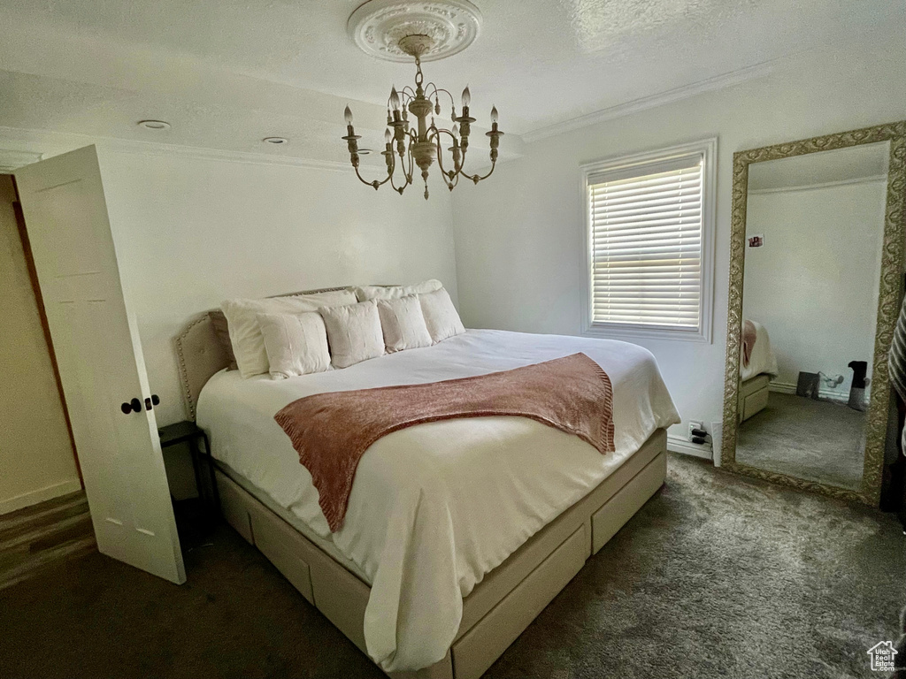 Bedroom with ornamental molding, dark colored carpet, a chandelier, a textured ceiling, and baseboards