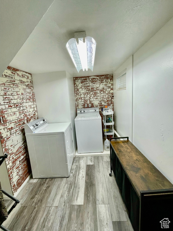 Laundry room featuring washer and clothes dryer, brick wall, and light wood-style floors