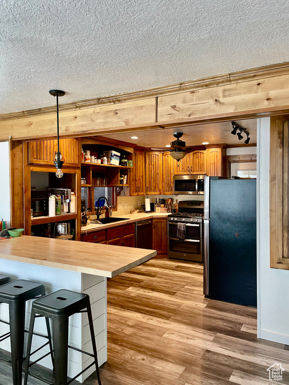 Kitchen with appliances with stainless steel finishes, a sink, a textured ceiling, light wood-style flooring, and brown cabinetry