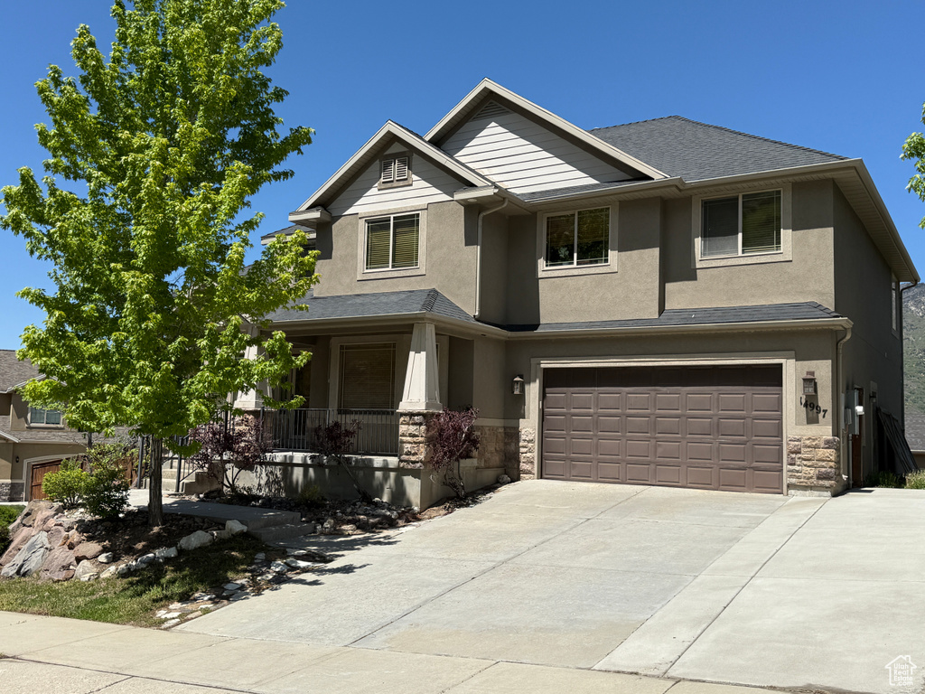 View of front of property with a porch, stone siding, stucco siding, concrete driveway, and a garage