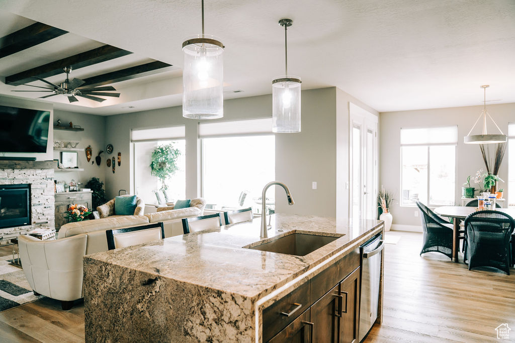 Kitchen featuring a sink, stainless steel dishwasher, light wood-style floors, open floor plan, and beam ceiling