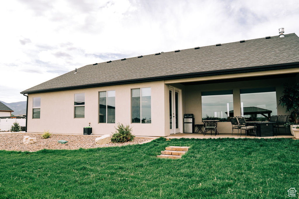 Rear view of house with a patio, a lawn, a shingled roof, and stucco siding