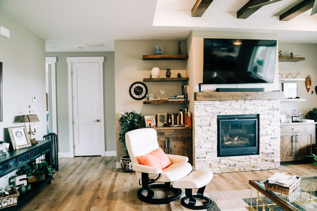 Living room with wood finished floors, a stone fireplace, and baseboards