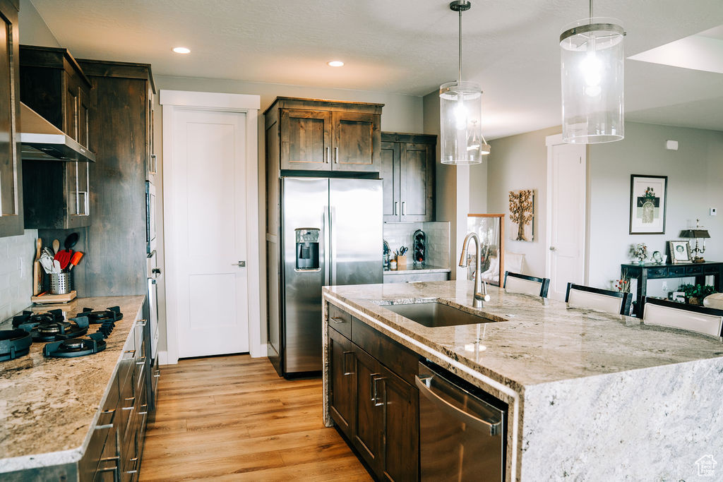 Kitchen featuring appliances with stainless steel finishes, a sink, backsplash, light wood-type flooring, and a center island with sink