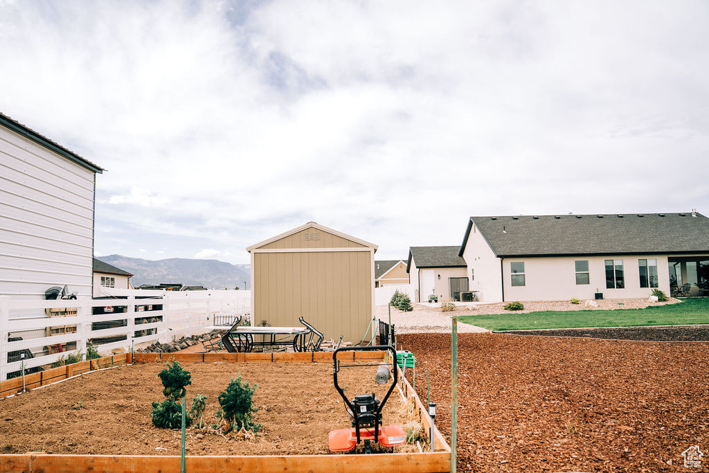 View of yard with a garden, fence, an outbuilding, a mountain view, and a storage shed