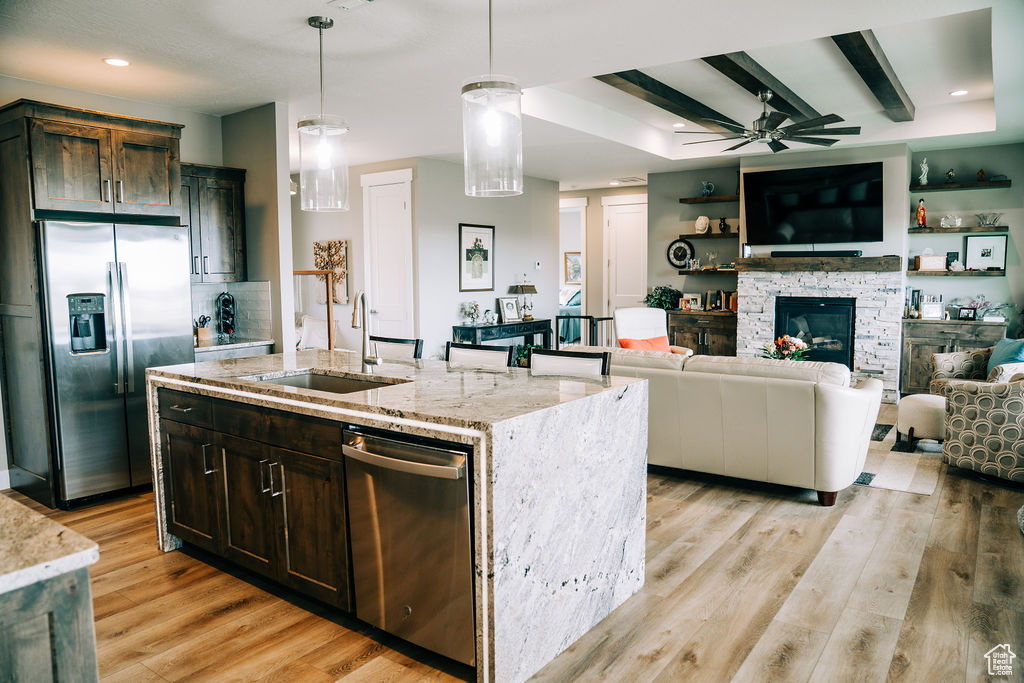 Kitchen with appliances with stainless steel finishes, a ceiling fan, a sink, light stone counters, and light wood-style floors
