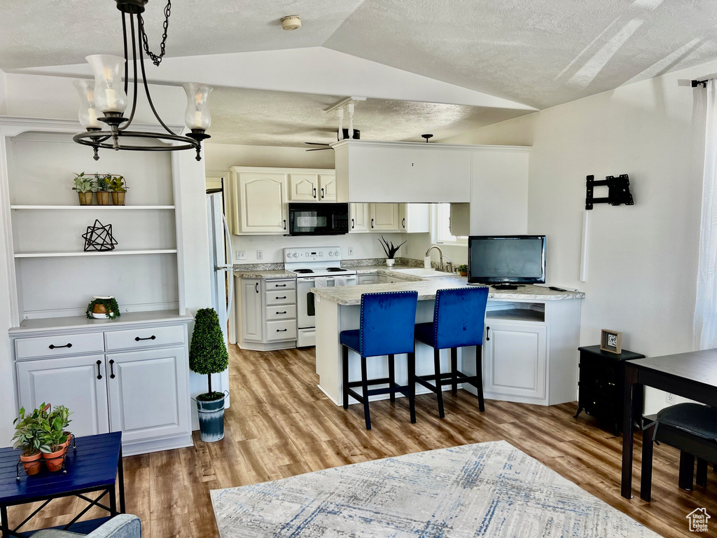 Kitchen featuring white appliances, a peninsula, a sink, open shelves, and lofted ceiling