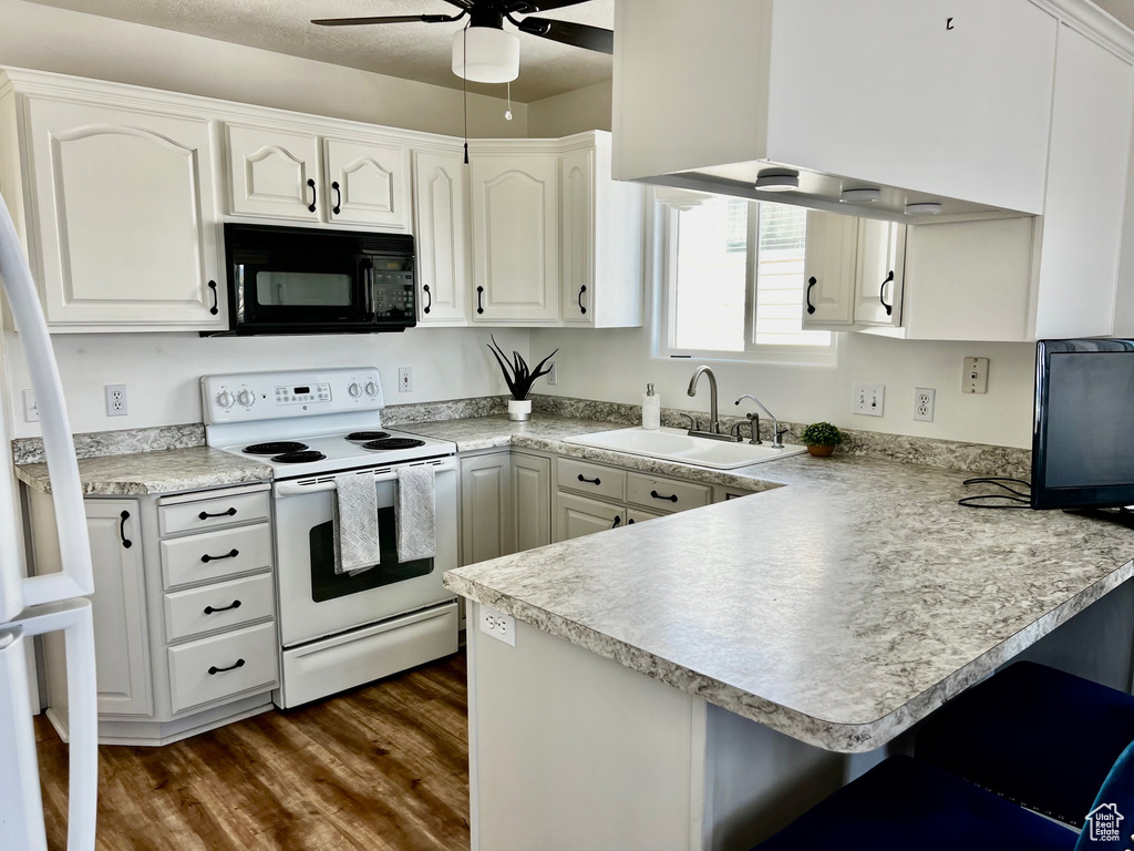 Kitchen with black microwave, white range with electric cooktop, a sink, a peninsula, and a ceiling fan
