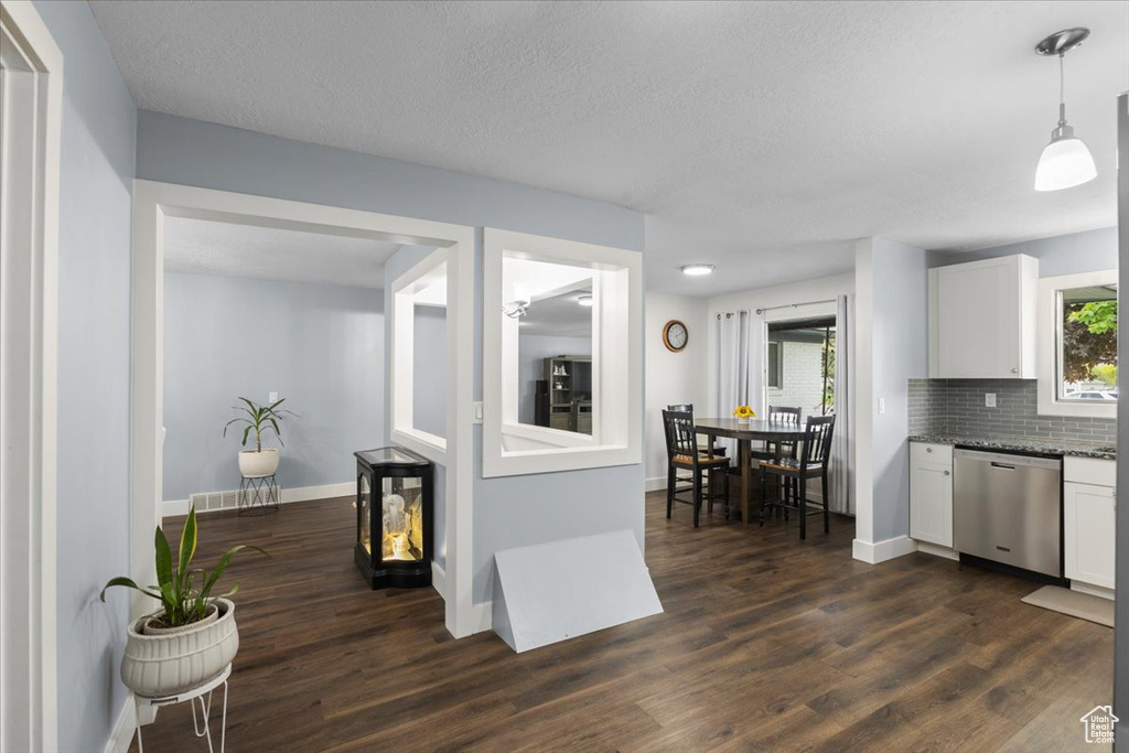 Kitchen with stainless steel dishwasher, white cabinets, dark wood-type flooring, backsplash, and baseboards