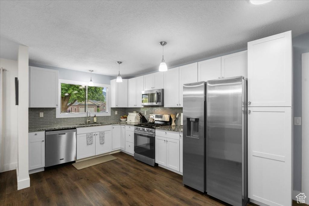 Kitchen featuring appliances with stainless steel finishes, a sink, decorative backsplash, white cabinetry, and dark wood-type flooring