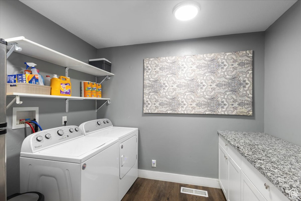 Clothes washing area with washing machine and dryer, dark wood finished floors, baseboards, and cabinet space