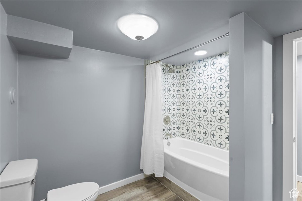 Bathroom featuring toilet, wood finished floors, shower / tub combo with curtain, and baseboards